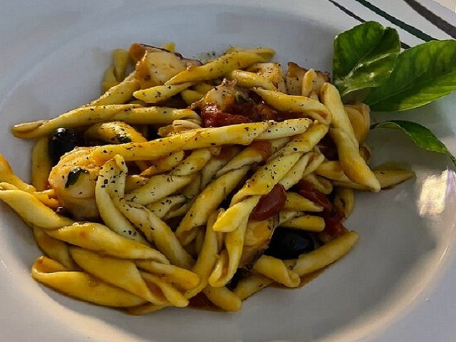Pasta fatta a mano con pomodoro, olive nere e una foglia di basilico