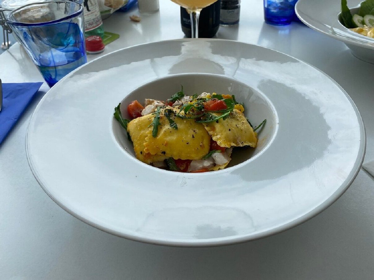 Ravioli con pomodorini ed erbe aromatiche, serviti su una tavola apparecchiata con bicchieri blu