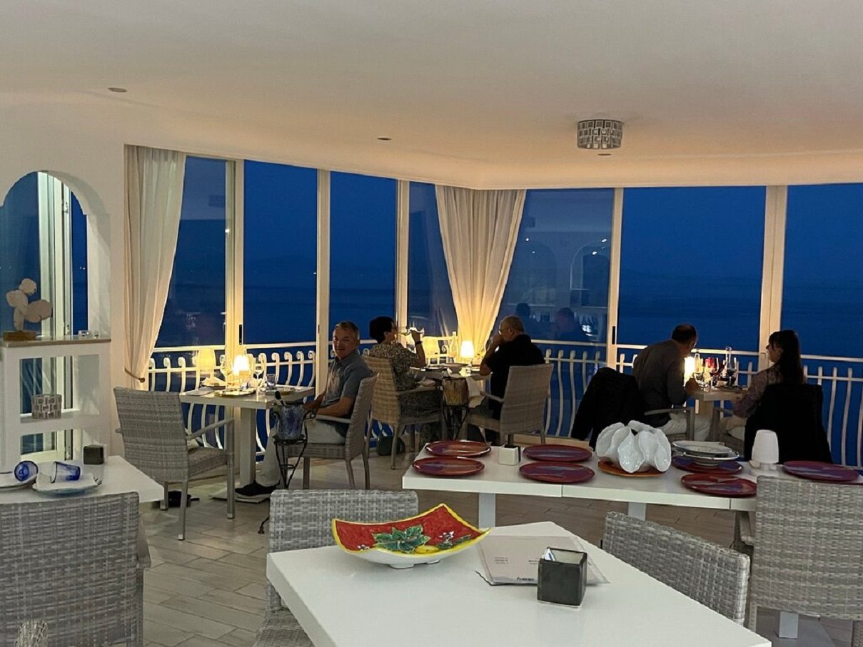 Sala di sera con tavoli a lume di candela e grandi finestre sul mare