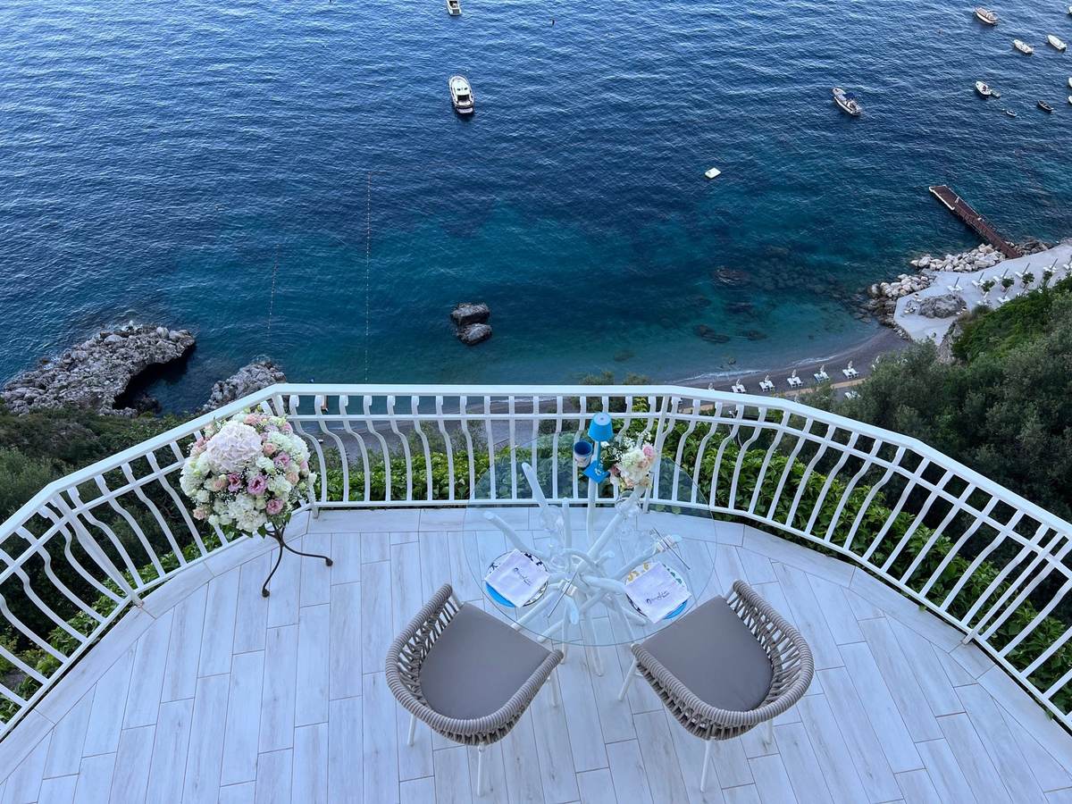 Terrazza privata apparecchiata per due sul mare, con le barche sull&rsquo;acqua più in basso